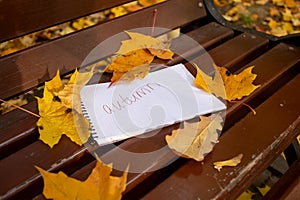 notepad with inscription autumn lies in park bench in autumn leaves in sun shining