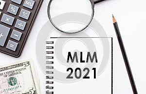 Notepad with MLM 2021 note on desk with calculator, dollars and magnifying glass. Multi Level marketing concept