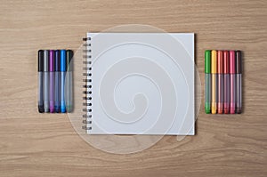 Notepad or notebook with Many colorful pens on brown wood table.using for education, business background