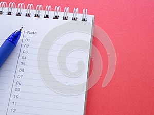 Notepad with numbers 01-12 and blue pen on a red workplace offiec background.