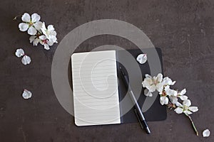 Notepad with pen and flowers of almond on a dark background. Co