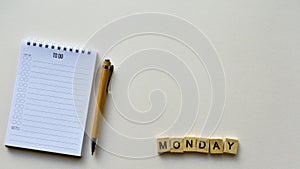 Notepad with pen and wooden word `Monday` on a beige paper background. Top view. Close-up.