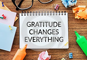 A notepad with the phrase GRATITUDE CHANGES EVERYTHING amidst colorful markers, glasses, and paper