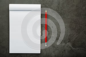 Notepad with a red pencil on a black stone plate background, for education, recording goals and deeds