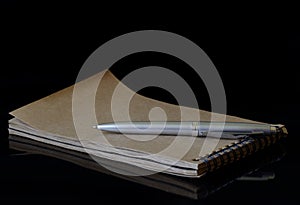 A notepad with a spring from eco-friendly recycled paper and a silver fountain pen lie on a dark background. Photo. Copy space