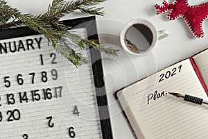 Notepad for taking notes of goals and plans for the new year, calendar,a cup of coffee, Christmas tree decorations on the desktop.