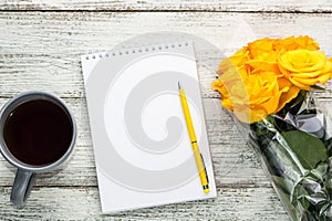 Notepad and tea with a bouquet of yellow roses on a white wooden background