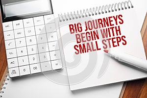 Notepad with text Big journeys begin with small steps on wooden background with calculator and red marker