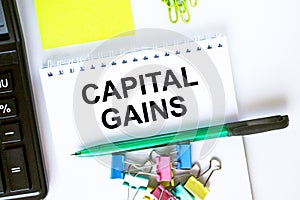 Notepad with text Capital Gains. Calculator, green pen stickers and stationary clips