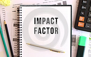 Notepad with text IMPACT FACTOR on the office desk, near office supplies. Business concept