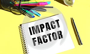 Notepad with text IMPACT FACTOR with stationery. Yellow background color.