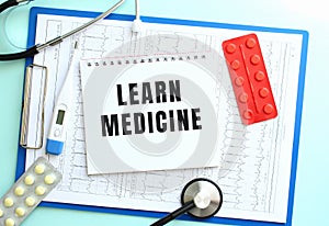 A notepad with the text LEARN MEDICINE lies on a medical clipboard with a stethoscope and pills on a blue background.