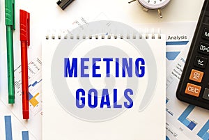 Notepad with the text MEETING GOALS on a color financial chart. Business concept