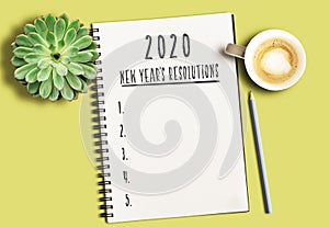 Notepad with text 2020 New Years Resolutions and numbered list on yellow desk with succulent plant and cup of coffee