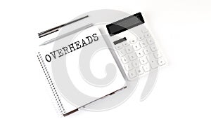 Notepad with text OVERHEADS with calculator and pen. White background. Business concept