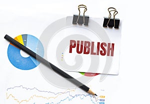Notepad with text PUBLISH on business charts and pen