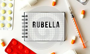 Notepad with text RUBELLA on a white background. Nearby are various medicines