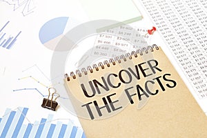 Notepad with text UNCOVER THE FACTS. Diagram and white background
