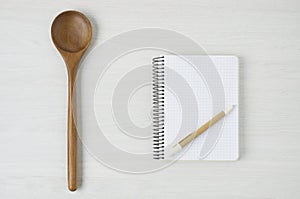 Notepad and wooden spoon on white wood table