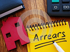 Notepad with word arrears and model of house.