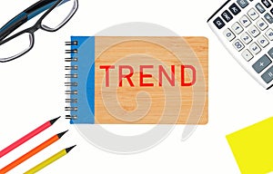 a notepad with the word Trend on a white background . Near glasses, calculator, pencils, paper for writing.
