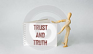 Notepad with the words TRUST and TRUTH on a light background with a wooden doll. Reliability, truth, beliefs and consent concept