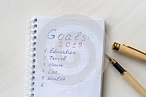 Notepad with written goals and pen on wooden desk