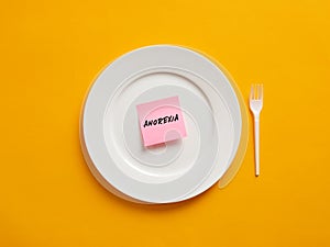 Notepaper with the word anorexia on a white plate. Eating disorder and unhealthy nutrition