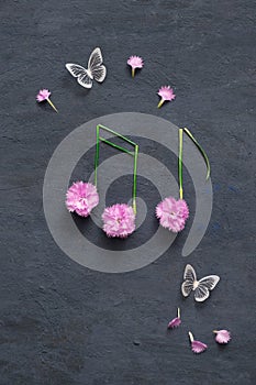 Notes of flowers and stems on a dark stone background with butterflies. Musical summer abstraction top view