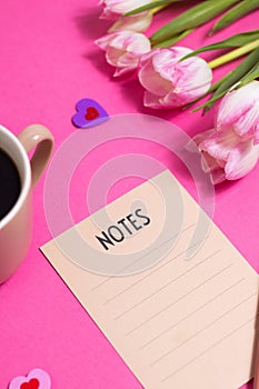 Notes with pen, cup of coffee, tulip spring flower and cute hearts on pink background, flat lay