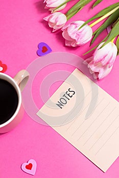 Notes with pen, cup of coffee, tulip spring flower and cute hearts on pink background, flat lay