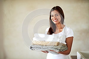 Nothing better than clean, fresh towels. Portrait of a happy young woman holding a pile of clean folded towels.