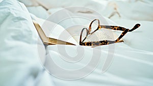 Nothing better than sliding into bed with a good read. Still life shot of a book and a pair of spectacles on a bed.