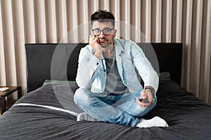 Nothing interesting to watch. Handsome young man holding remote control and looking bored while watching TV on the couch at home