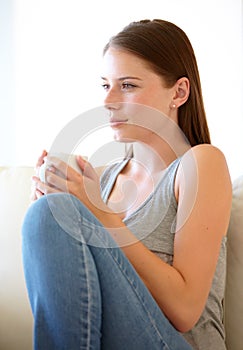 Nothing like a morning cuppa. A gorgeous young woman sitting on the couch with a cup of coffee.