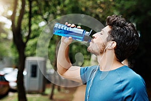 Nothing like water to refuel the engine. a sporty young man drinking water out of a bottle after having a jog outside