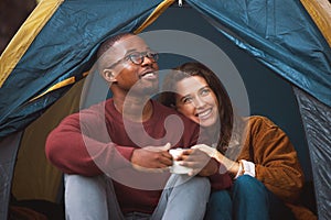 Nothing says romance like a tent, chirping birds and bae. a young couple drinking coffee while sitting in their tent.