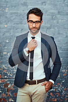 Nothings out of place. Cropped portrait of a handsome young businessman adjusting his tie while standing against a grey