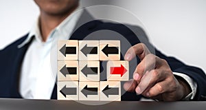 The notion of a businessman\'s hand holding a wooden block with a red arrow pointing in one direction and a black arrow.