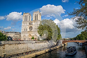 Notre Dame de Paris in a sunny day, view from the rive Seine with tourists and cruise