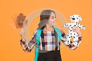 Nourish child with game. Small child hold toy doll and autumn leaves. Little girl play game in school. Game and learning