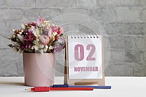 november 02. 02-th day of the month, calendar date.A delicate bouquet of flowers in a pink vase, two pencils and a