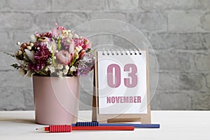 november 03. 03-th day of the month, calendar date.A delicate bouquet of flowers in a pink vase, two pencils and a