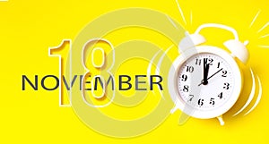 November 18th. Day 18 of month, Calendar date. White alarm clock with calendar day on yellow background. Minimalistic concept of