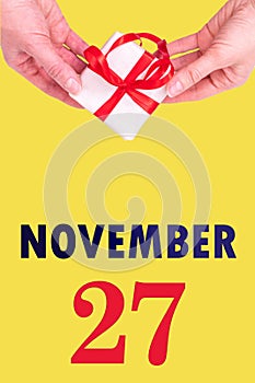 November 27th. Festive Vertical Calendar With Hands Holding White Gift Box With Red Ribbon And Calendar Date