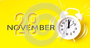November 28th. Day 28 of month, Calendar date. White alarm clock with calendar day on yellow background. Minimalistic concept of