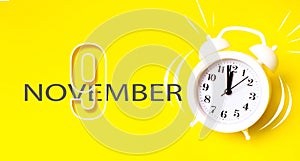 November 9th. Day 9 of month, Calendar date. White alarm clock with calendar day on yellow background. Minimalistic concept of