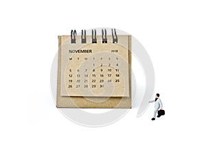 November. Calendar sheet and miniature plastic businessman on white background.