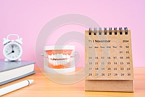 November monthly desk calendar for 2024 year and model dentures on the table with alarm clock