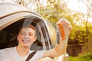 Novice driver holding car keys out of the window and smiling. New driver on the road concept